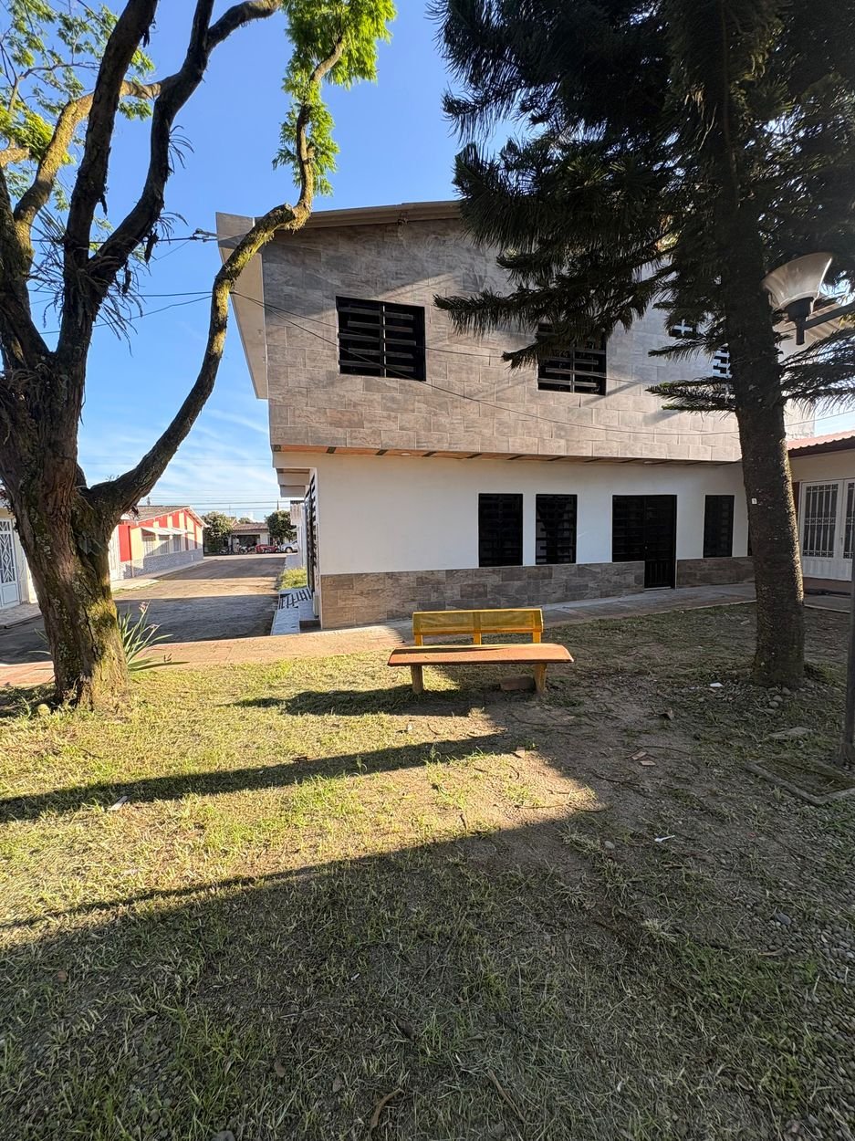 La casa de Floral Home Acacías vista desde la zona verde del Parque Infantil Las Acacias, con una banca a la sombra de los árboles